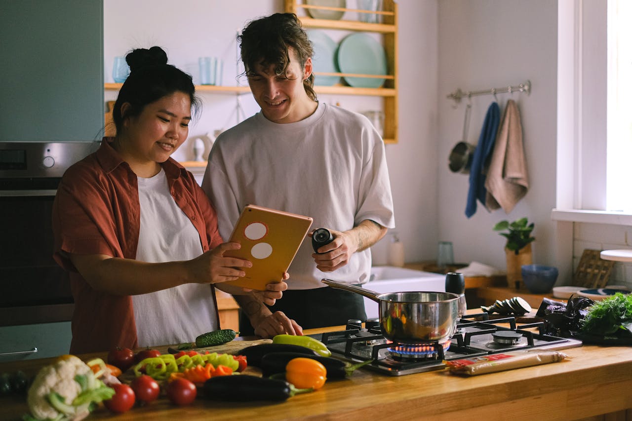 gallery-01 A couple preparing a meal together using a tablet in a modern kitchen setting.